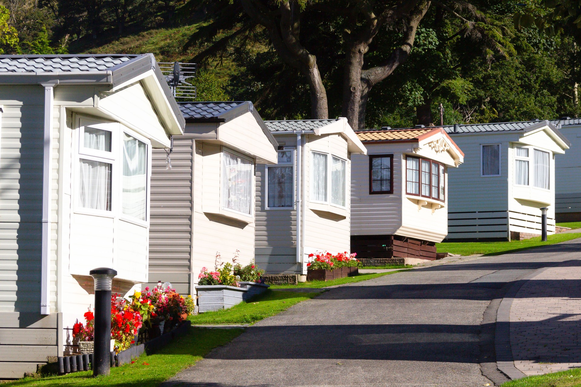 Row of mobile home caravans viewed from bottom of hill on a summers day with pots of flowers creating a welcoming home from home for people on vacation escaping for a break from the rat race.